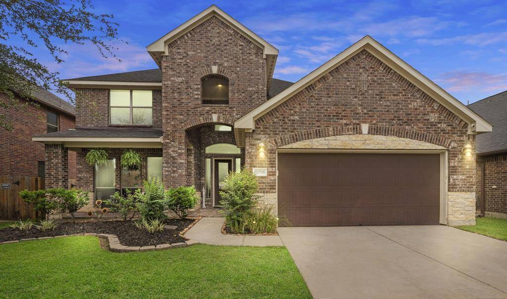 This beautiful two-story home features a classic brick exterior with a gabled roof. It includes a spacious two-car garage and a well-maintained front yard with lush greenery, offering great curb appeal.