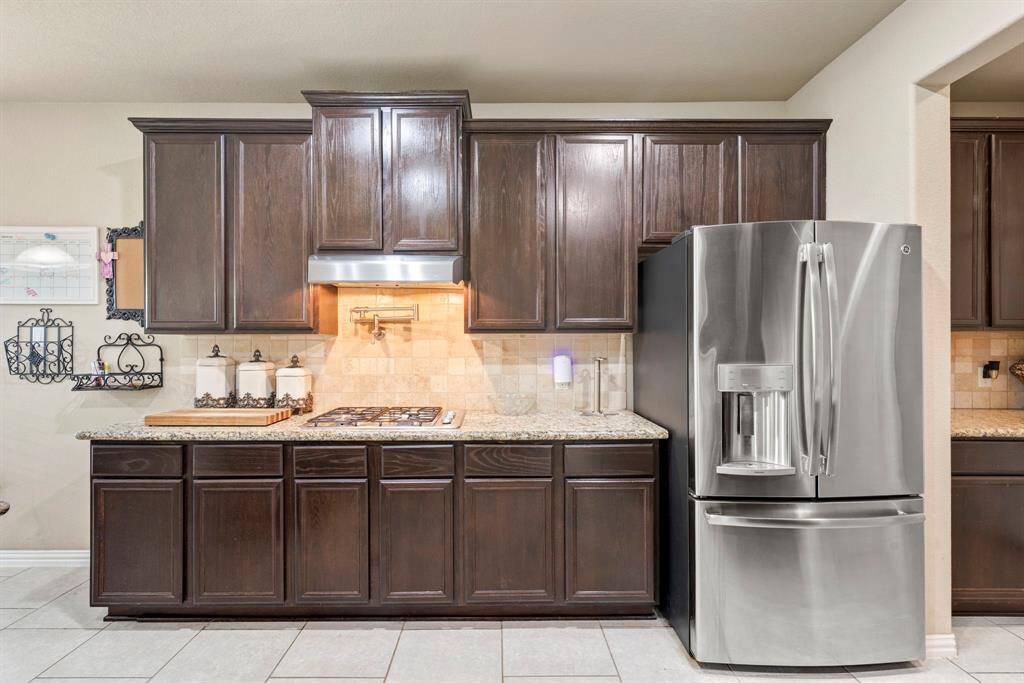 This kitchen features elegant dark wood cabinets, granite countertops, and a modern gas cooktop with a stylish vent hood, creating a functional and attractive cooking space.