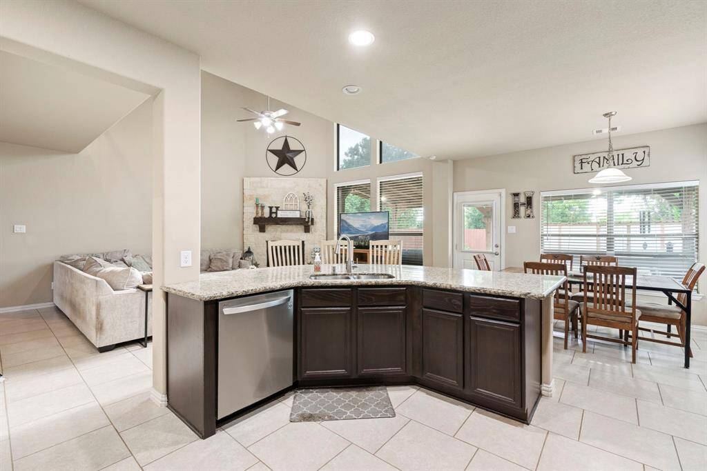 This spacious open-concept kitchen and living area features a large island with granite countertops, modern appliances, and ample cabinetry. The living room has high ceilings and plenty of natural light, with a cozy seating area. Adjacent is a breakfast area with a large window and patio door, perfect for family gatherings.
