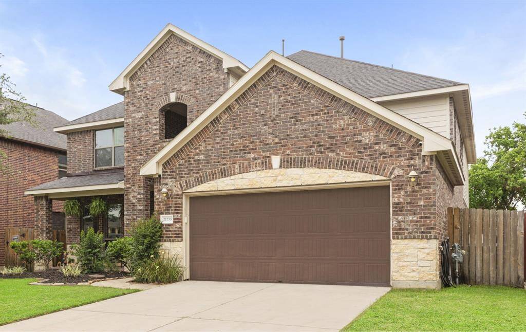 This charming brick home features a well-maintained front yard with lush greenery and a mature tree. The house includes a two-car garage and a welcoming front porch, creating excellent curb appeal.