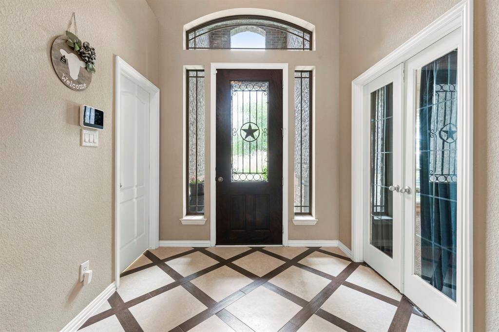 This entryway features a dark wood door with decorative glass and sidelights, flanked by double glass doors on the right to the study/extra bedroom. The space is accented by a patterned tile floor and neutral walls, offering a welcoming and elegant first impression.