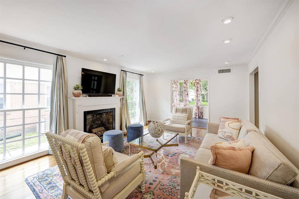 This view of the spacious living room with recessed lights offers a glance into the sunroom to the south. The fireplace and mantle add architectural interest to this light-filled lounging area.