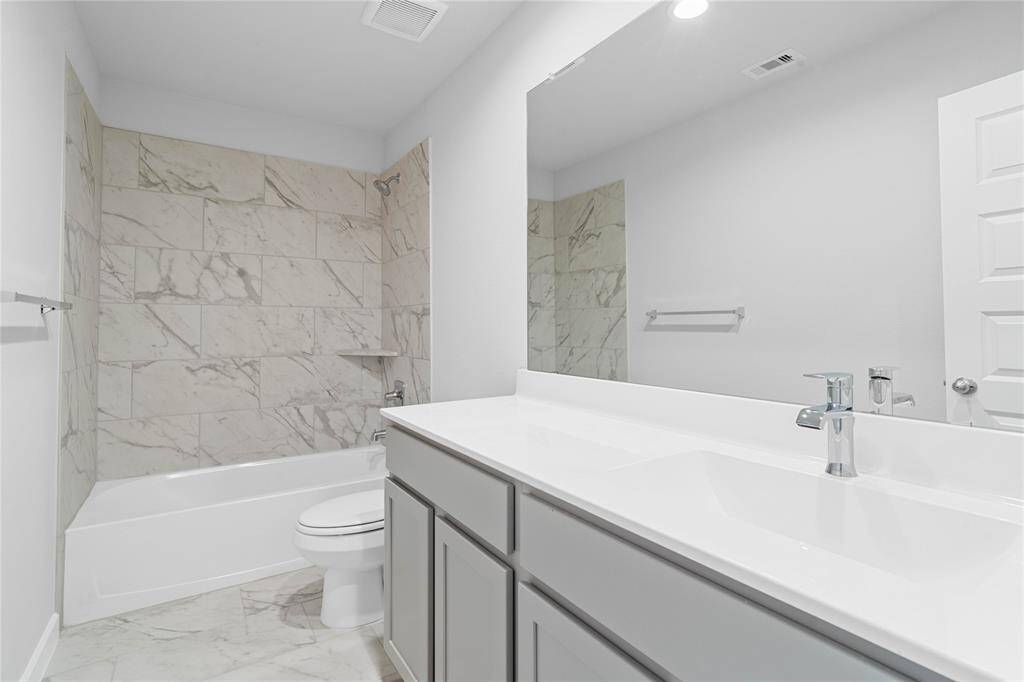 Secondary bath features tile flooring, bath/shower combo with tile surround, stained wood cabinets, beautiful light countertops, mirror, dark, sleek fixtures and modern finishes!