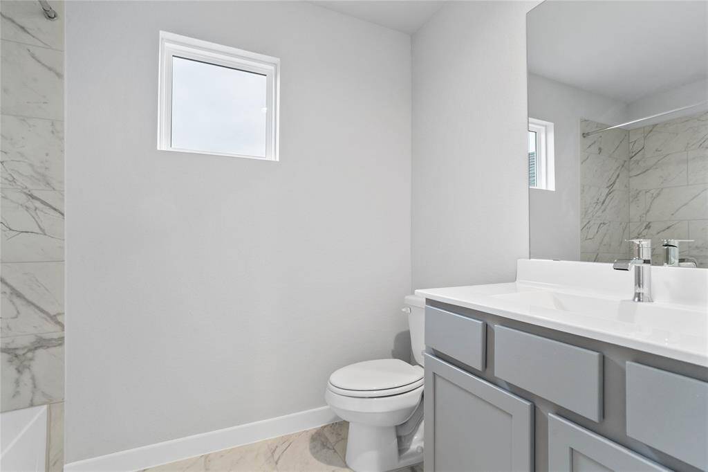 Secondary bath features tile flooring, bath/shower combo with tile surround, stained wood cabinets, beautiful light countertops, mirror, dark, sleek fixtures and modern finishes!