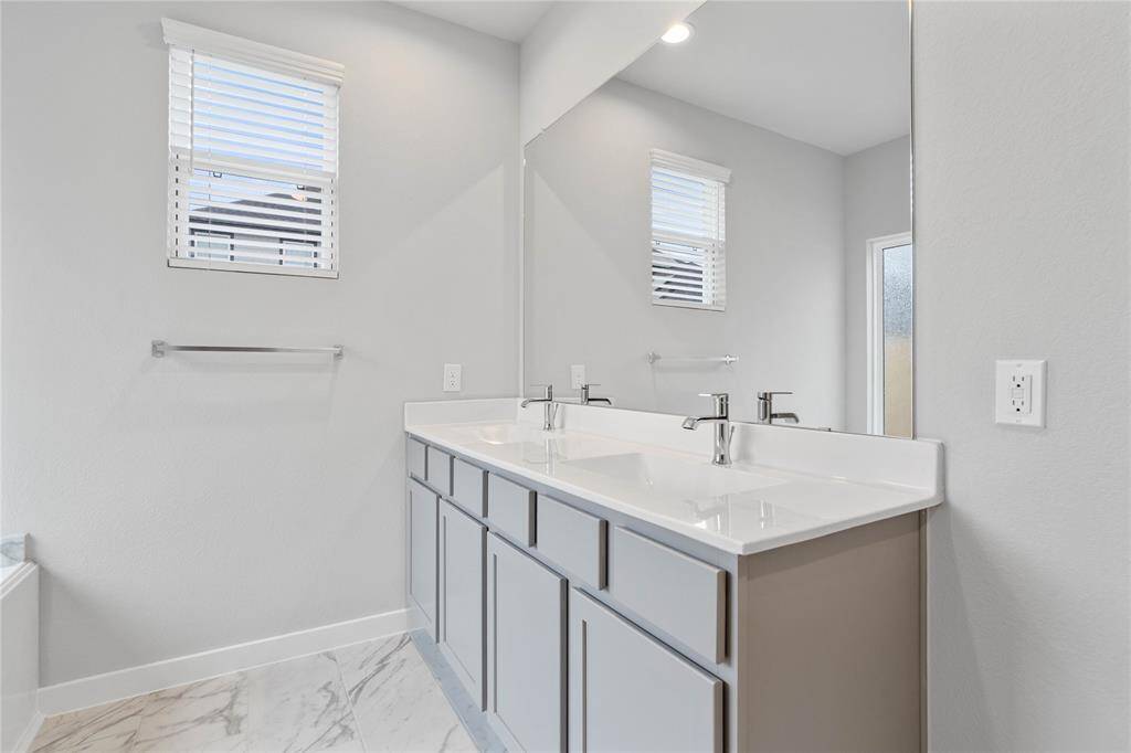 Wow! Look at this primary bathroom! Complete with stained cabinets with sleek light countertops and dual vanities, large modern tile flooring, large garden tub and walk-in shower with tile surround, and a window allowing in the natural light.
