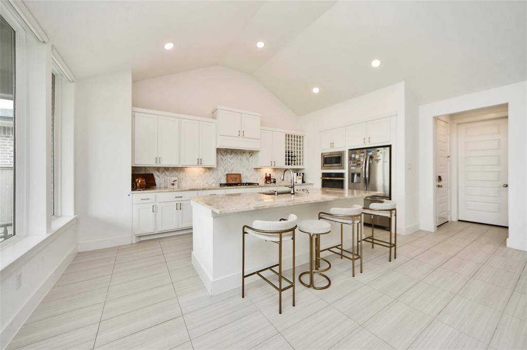 Elegant kitchen featuring crisp white cabinetry, stainless appliances, herringbone backsplash, and a large island with seating.
