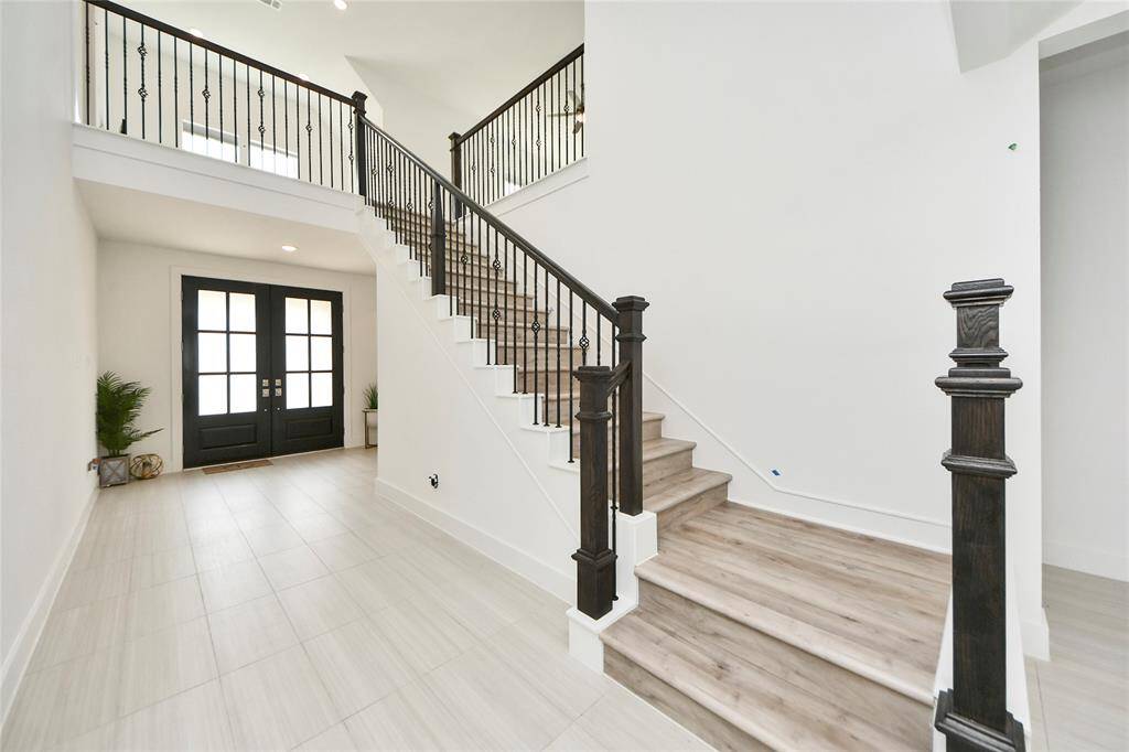 Elegant staircase with dark wood railing and iron spindles, paired with a modern double-door entry for a grand first impression.
