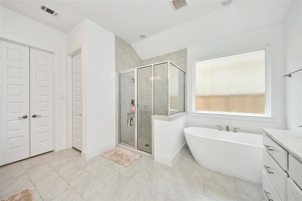 Luxurious primary bath with freestanding soaking tub, large walk-in shower, and frosted window for natural light and privacy.