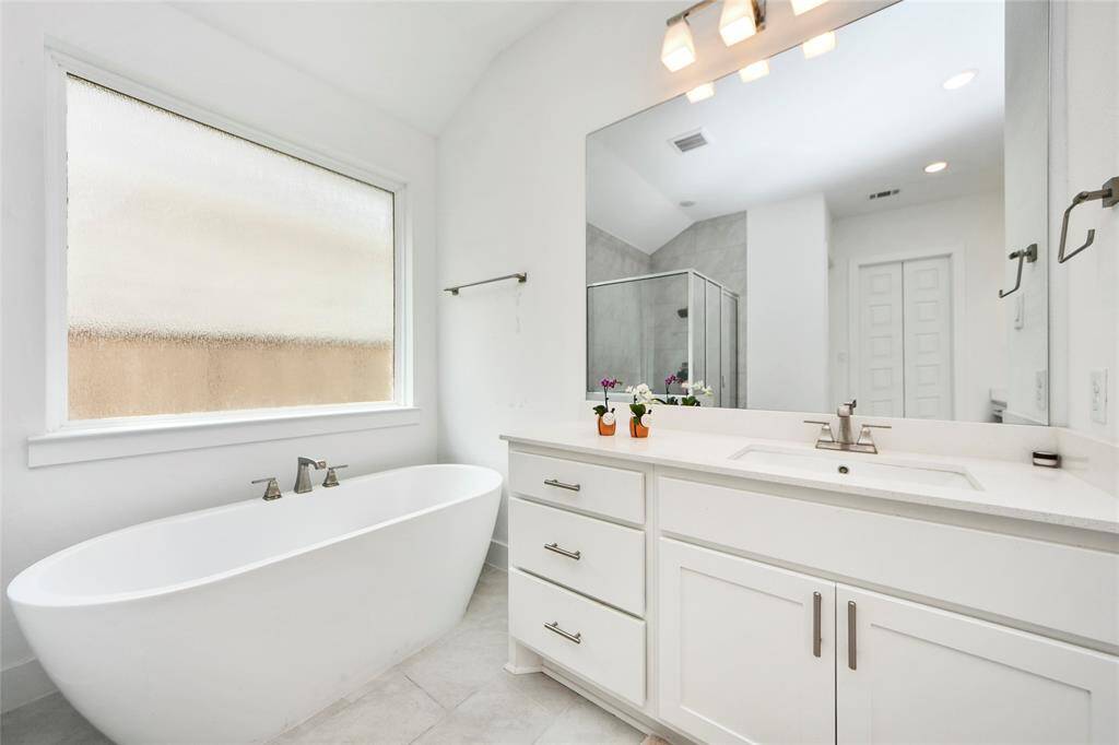 Dual-sink vanity with modern lighting and storage, paired with a deep soaking tub—your own personal spa retreat.