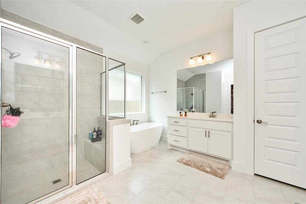 Another angle of the elegant primary bathroom highlighting the oversized walk-in shower with bench and frameless glass.