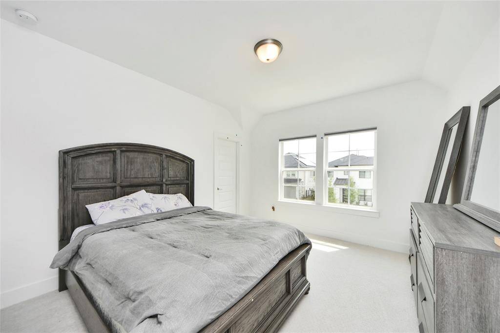 A cozy upstairs bedroom showcasing plush carpeting, neutral tones, and oversized windows offering peaceful neighborhood views.