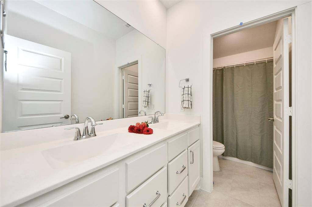 Sleek bathroom featuring a double sink vanity, large mirror, and a private bath/shower combo in a separate space for added functionality.