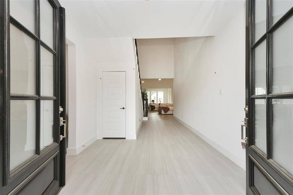 Step through elegant double doors into a bright, open hallway with soaring ceilings and sleek tile floors—setting the tone for the rest of the home.