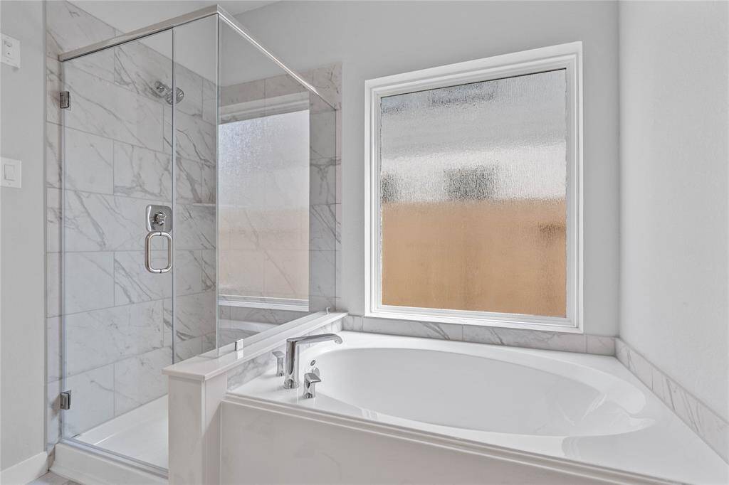 Additional view of the primary bathroom which features a large walk-in shower with tile surround, garden tub to soak after a long hard day, large window allowing in the natural light, rain glass window, custom paint, sleek and modern finishes.