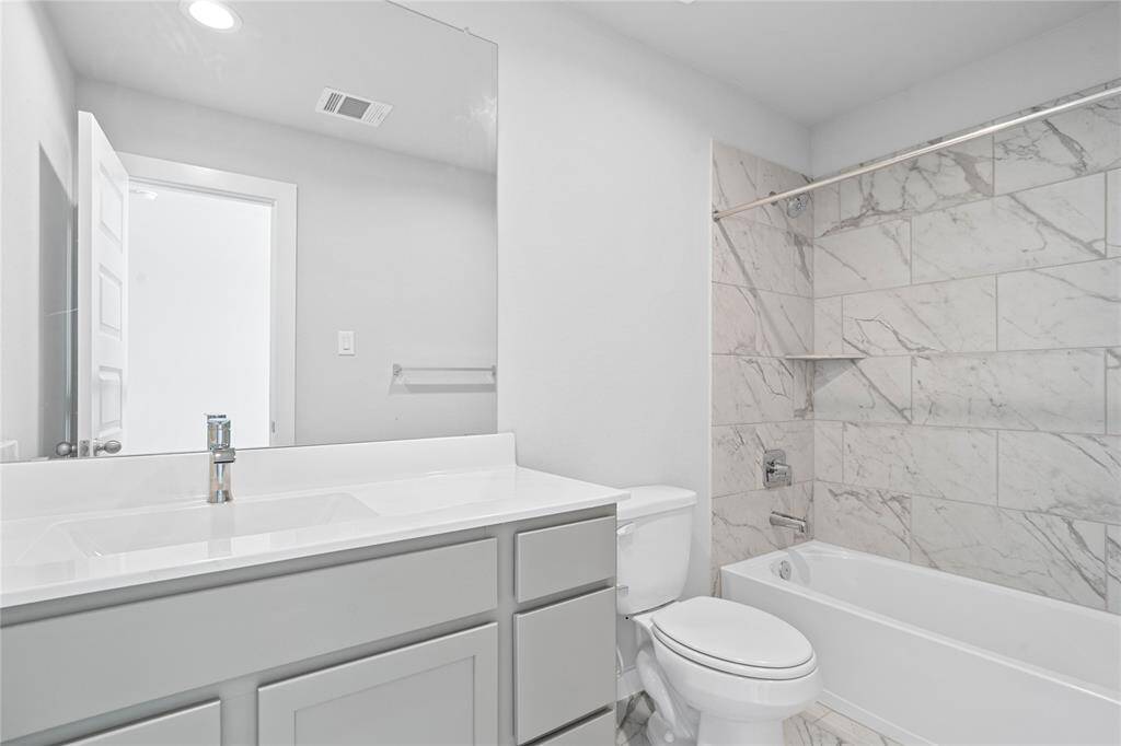 This secondary bath is off a secondary bedroom and features tile flooring, bath/shower combo with tile surround, stained wood cabinets, beautiful light countertop, mirror, sleek fixtures, and modern finishes.