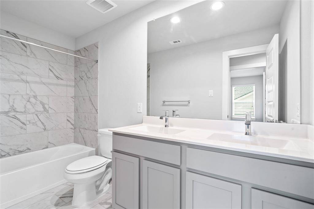 Secondary bath features tile flooring, bath/shower combo with tile surround, stained wood cabinets, beautiful light countertops with dual sinks, mirror, sleek fixtures and modern finishes.