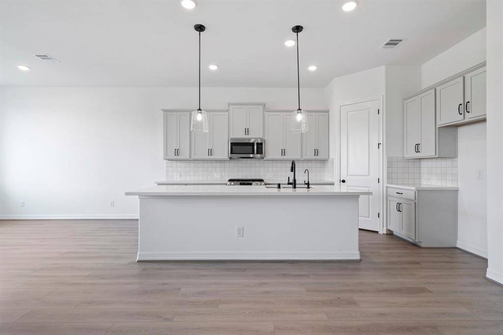 This light and bright kitchen features a large quartz island, white cabinets, a large sink overlooking your family room, recessed lighting, and beautiful backsplash.
