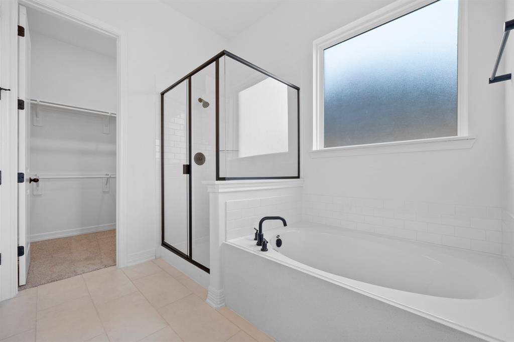 This additional view of your primary bathroom features tile flooring, fresh paint, walk-in shower, a separate garden tub, and a large walk-in closet.