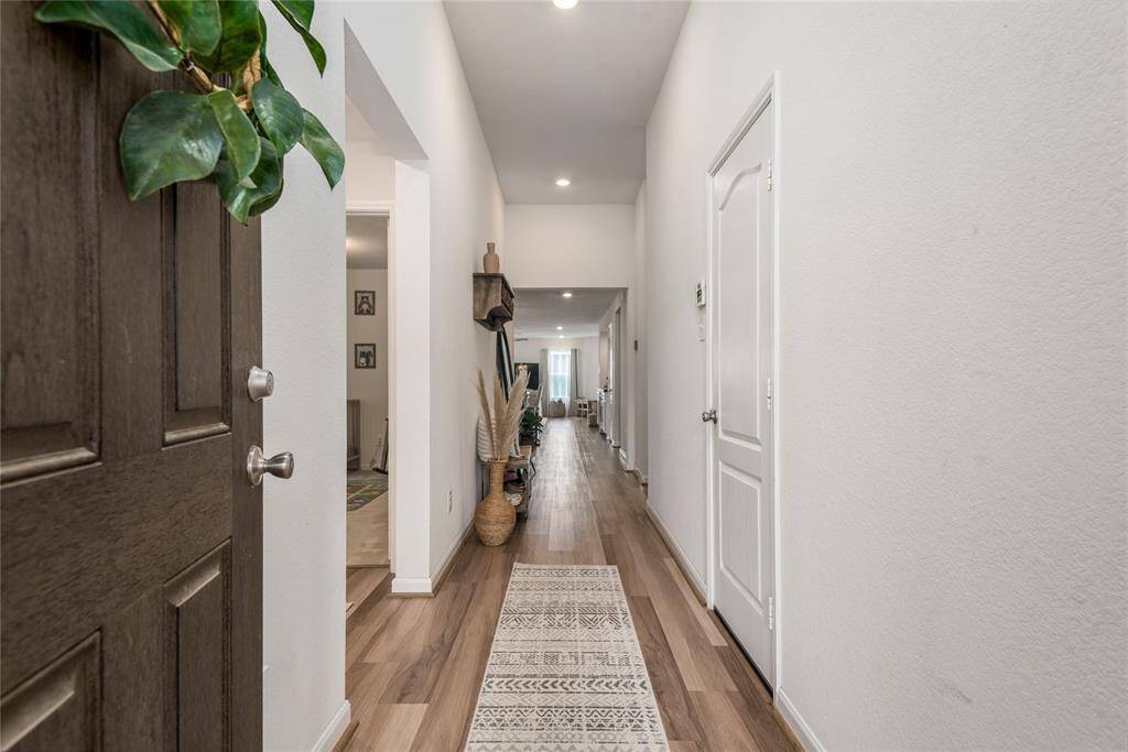 This photo showcases a welcoming hallway with wood flooring and neutral walls, leading to a bright living area. Cozy and inviting entryway!