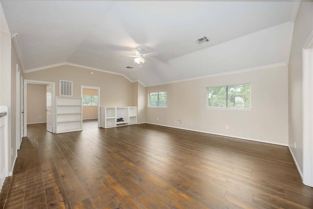 Spacious room with hardwood floors, neutral walls, and a sloped ceiling. Features built-in shelving and large windows offering natural light, ideal for a versatile living area.