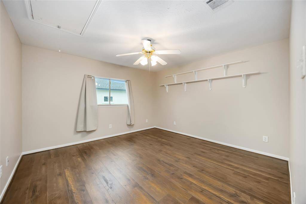 This room features a clean, minimalist design with hardwood floors, neutral walls, a ceiling fan, and natural light from a window with simple curtains. Built-in shelves provide extra storage space.