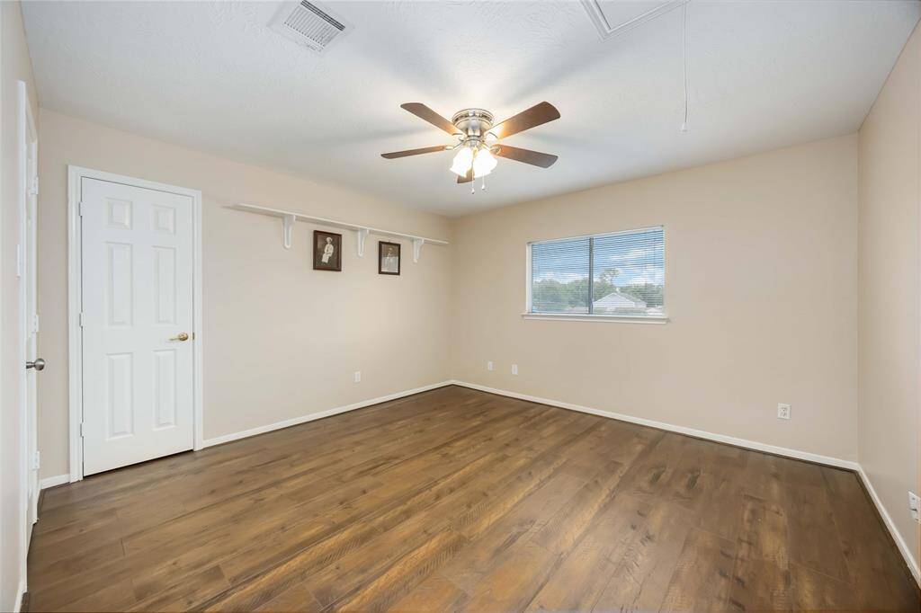 This spacious room features hardwood flooring, neutral walls, and a ceiling fan. It has a large window for natural light and a closet with a white door, making it ideal for a bedroom or office.
