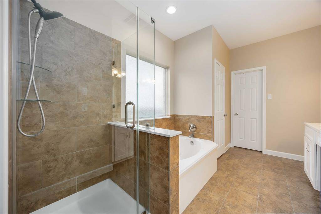 Modern bathroom with a glass-enclosed shower and a separate bathtub. It features neutral tile flooring and walls, a frosted window for privacy, and ample lighting.