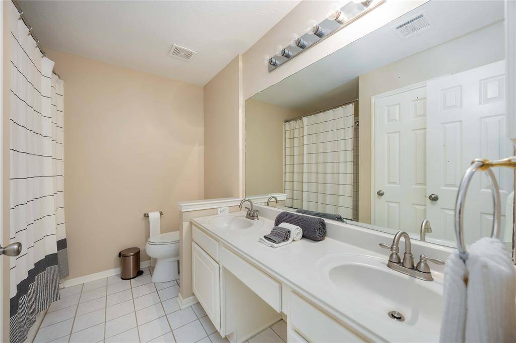 This bathroom features a double vanity with a large mirror, a shower-tub combo with a striped curtain, neutral walls, and tiled flooring for a clean, modern look.