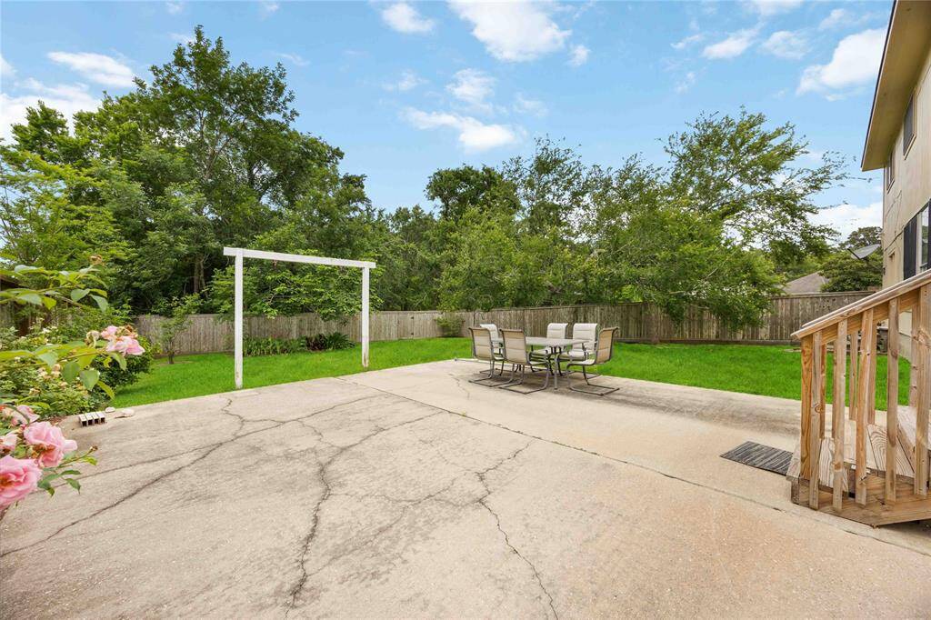 Spacious backyard with a large concrete patio, perfect for outdoor dining and entertaining. The area features a lush lawn, mature trees for privacy, and a wooden fence. Ideal for family gatherings and relaxation.