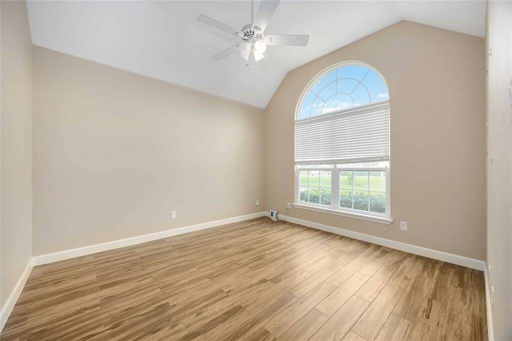 This bright room is the study and it offers vaulted ceiling, neutral walls, and wood-look flooring. Features a large arched window with blinds and a ceiling fan.