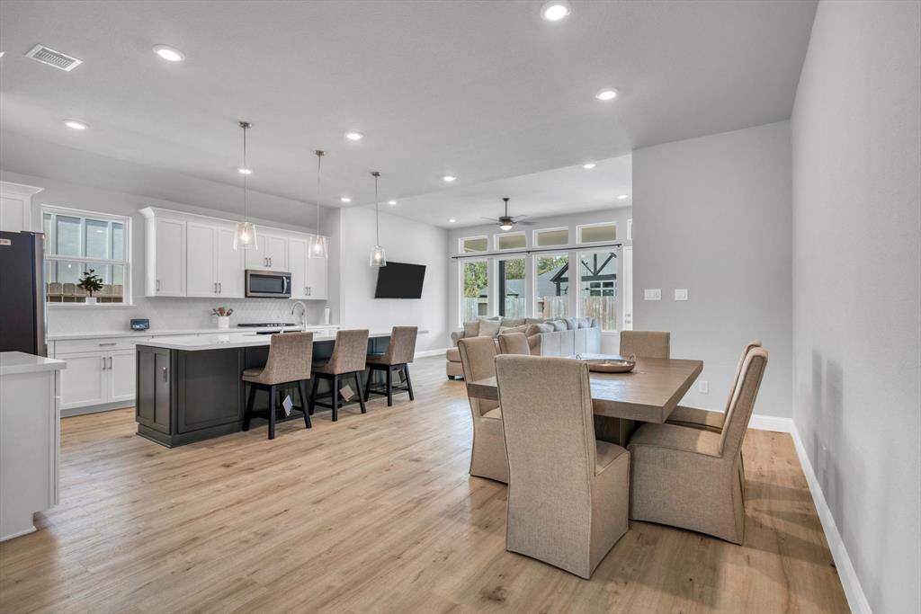 Spacious open-concept kitchen and dining area with modern finishes. The kitchen features a large island with seating, pendant lighting, and ample cabinet space.  This room is bright with natural light from large windows and offers a view of a landscaped backyard.