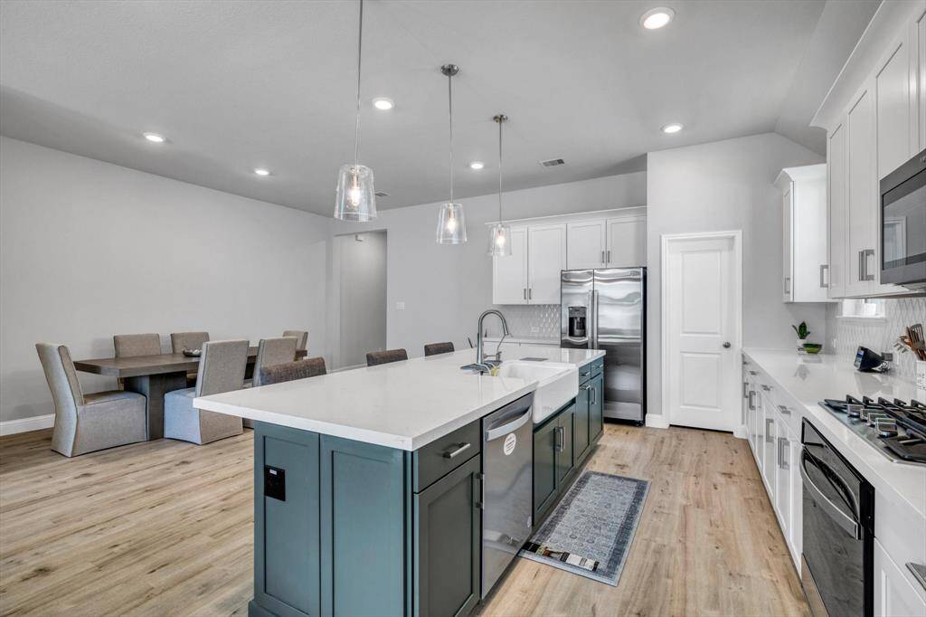 This modern kitchen features a spacious island with seating, sleek countertops, and stainless steel appliances. It opens to a dining area with ample natural light, perfect for entertaining.