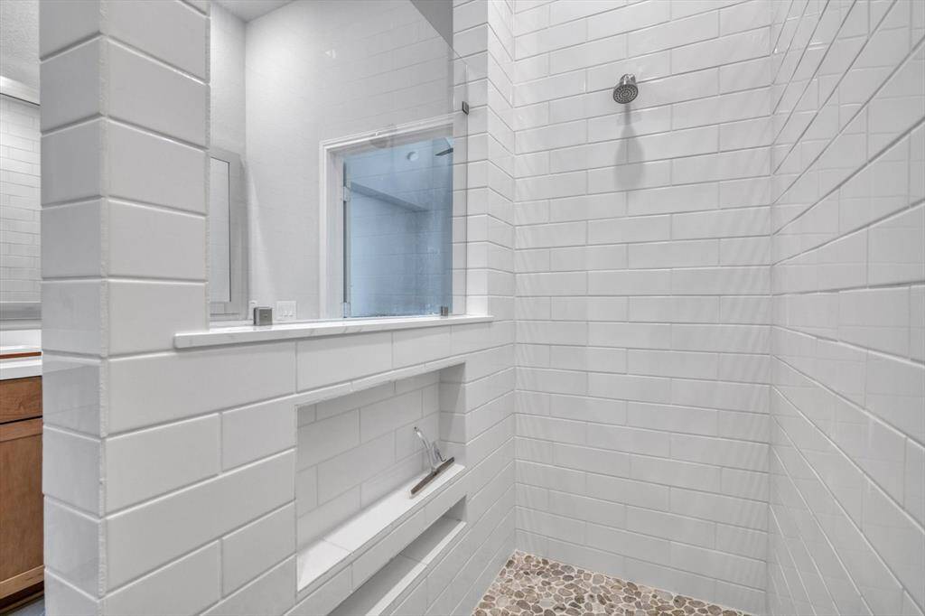 Modern bathroom shower with sleek white subway tiles and a pebble stone floor. It features a built-in niche for storage and a glass partition for a stylish, open feel.
