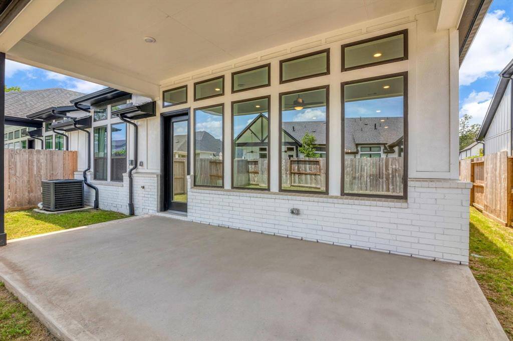 A covered patio area with large windows and a door leading inside. The space is bordered by a wooden fence and has a clean, modern look with a white brick exterior. Ideal for outdoor relaxation and entertaining.