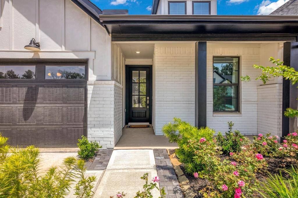This modern home features a sleek black and white exterior with a welcoming front porch, stylish black garage door, and well-maintained landscaping that includes vibrant greenery and colorful flowers.