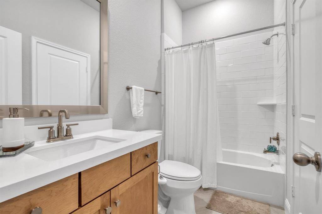 This is a modern bathroom featuring a sleek vanity with a large mirror, a bathtub with a shower and white tile, and a neutral color palette for a clean, bright look.