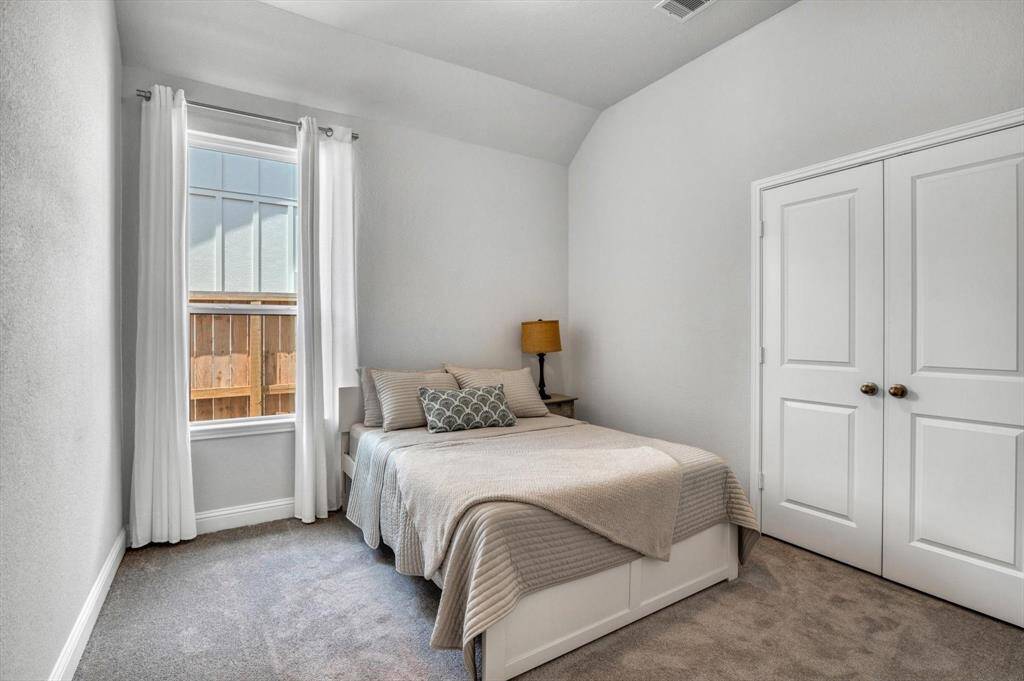 Secondary bedroom features a double-door closet for storage, with neutral color, and a large window with white curtains.