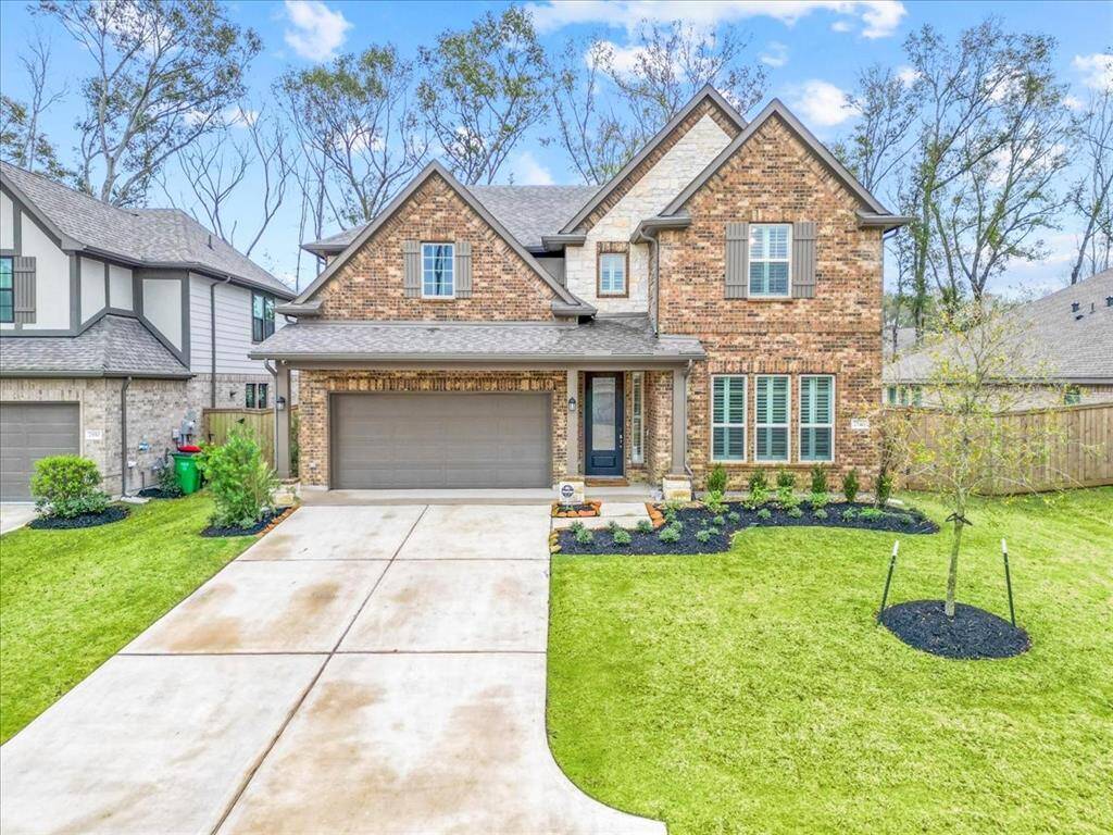 This photo showcases a beautiful two-story brick home with a spacious driveway and attached garage. The well-maintained front yard features fresh landscaping and an Oak tree. It's situated in The Highland's community with similar styled homes, offering a welcoming and serene atmosphere. This picture was taken right after a rainstorm, the driveway still appears a little wet in the pictures.