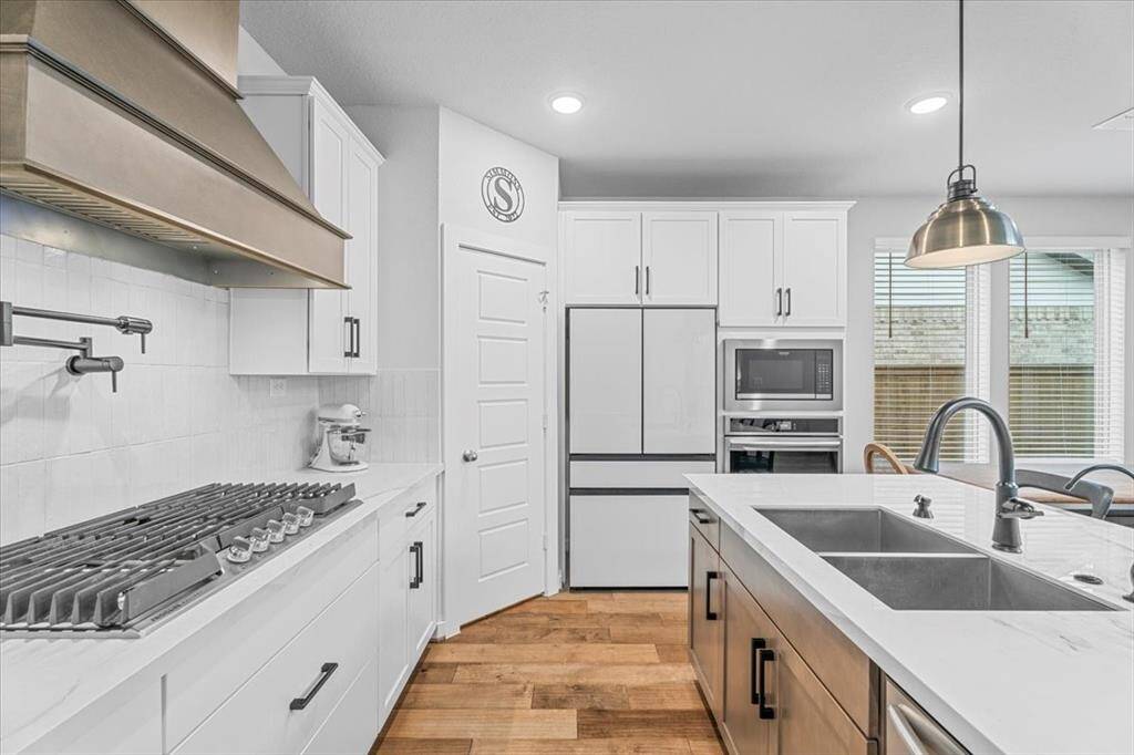 This modern kitchen features sleek white soft-close cabinetry, a large island with a double sink, and stainless-steel appliances. It has a gas cooktop, built-in oven, and ample natural light from large windows, creating a bright and inviting space.