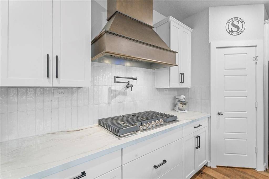 Modern kitchen with a sleek finish. Features a convenient pot filler, quartz countertops, and a stylish tile backsplash. Bright and functional space for cooking enthusiasts.