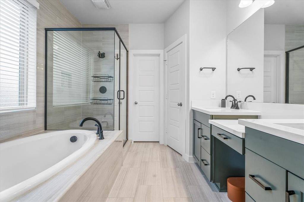 This modern bathroom features a spacious glass-enclosed shower, a large soaking tub, and dual sinks with sleek fixtures. The light wood flooring and neutral tones create a bright and inviting atmosphere.