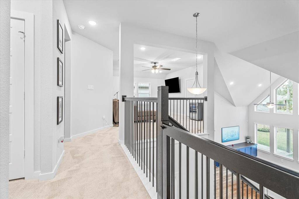 This photo showcases a bright, open upstairs area with carpeted flooring and a modern railing overlooking a spacious living room. Large windows provide ample natural light, and a ceiling fan adds a contemporary touch.