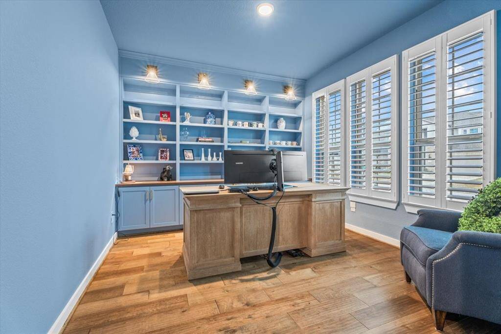 Embrace your work from home days with this large office, featuring custom lights, with built-in shelves and custom interior plantation shutters. This home office features elegance and creates a soft work from home environment.
