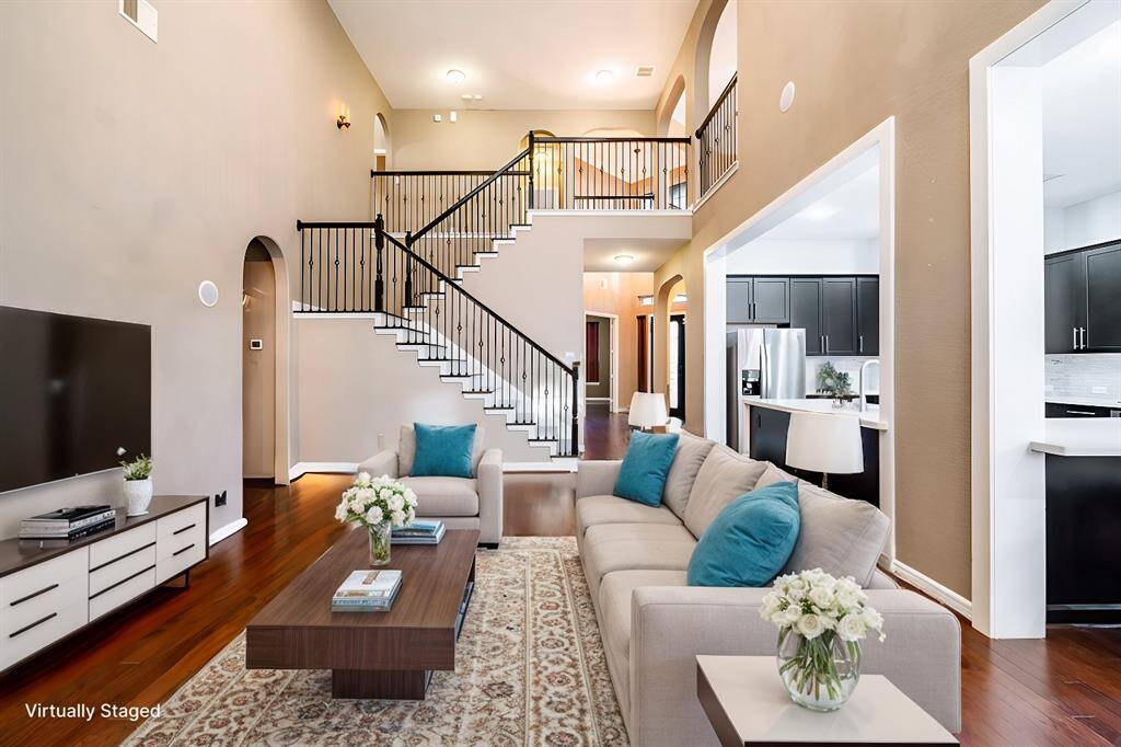 This elegant living space features an open floor plan with warm hardwood floors and a striking wrought iron staircase as the centerpiece. High ceilings and arched entryways enhance the spacious feel, while the modern kitchen and living area seamlessly connect, making it perfect for entertaining.