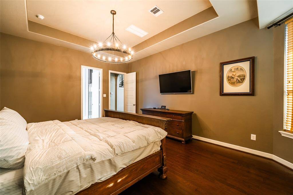 This luxurious primary bedroom features a stunning **Restoration Hardware chandelier** that adds elegance to the tray ceiling design. The warm hardwood floors complement the timeless **St. James furniture set**, which is also available for sale. Large windows and neutral tones create a cozy yet sophisticated retreat.