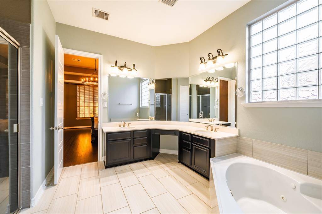 This luxurious primary bath offers a serene retreat with a jetted tub and a separate glass-enclosed shower. Dual vanities with ample counter space and stylish lighting provide both elegance and functionality. Annexed to the primary bedroom, it also features direct access to a spacious walk-in closet for ultimate convenience and organization. The large glass block window brings in natural light while maintaining privacy, completing this spa-like experience.