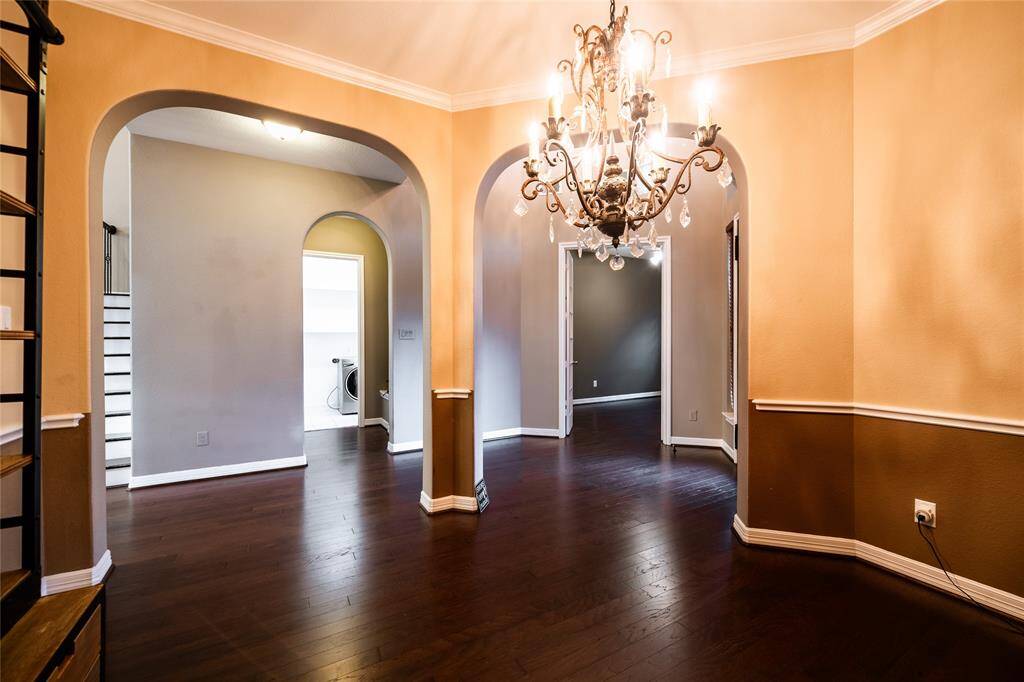 The dining/living space seamlessly combines functionality and style, showcasing rich hardwood floors and warm, neutral walls with wainscoting accents. a classic chandelier adds a touch of sophistication to the inviting ambiance.