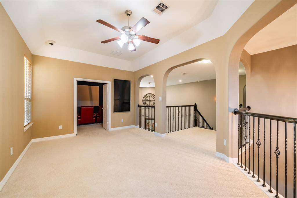 This versatile family/game room offers an open and inviting space with soft carpeting, tray ceilings, and large windows for natural light. The room's layout provides easy access to adjacent spaces, including the private home theater. Wrought iron railings and arched entryways add elegance, making it perfect for relaxation, gaming, or entertaining.