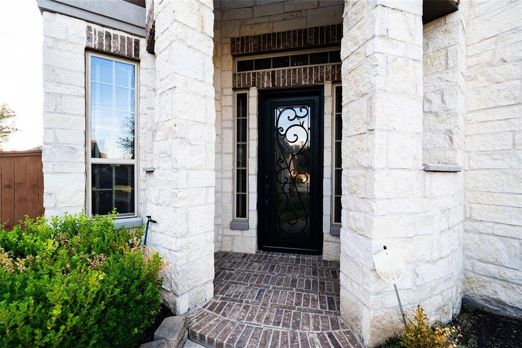 This elegant entrance features a beautifully designed wrought iron door surrounded by stone accents, creating a grand and welcoming aesthetic. Enhanced with a modern surveillance camera and intercom system, this entrance not only provides curb appeal but also ensures added security and convenience for homeowners.