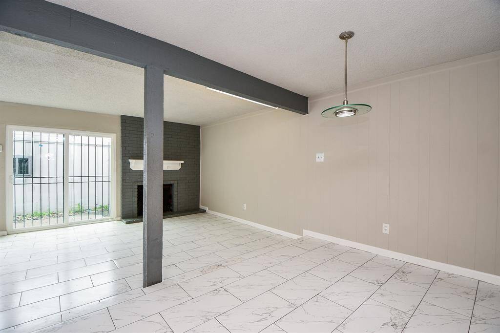 This room features a spacious open layout with light tile flooring and neutral walls. It includes a cozy brick fireplace, sliding glass doors leading outside, and a modern ceiling light fixture. Ideal for a living or dining area.